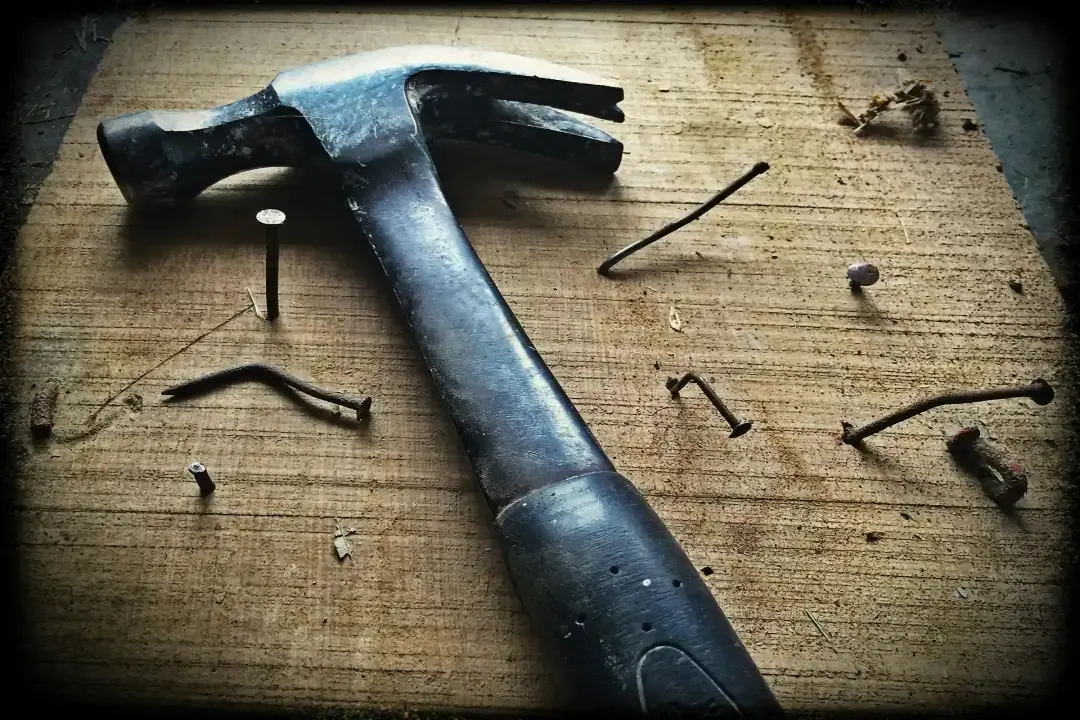 A hammer with nails pushed into the wood.
